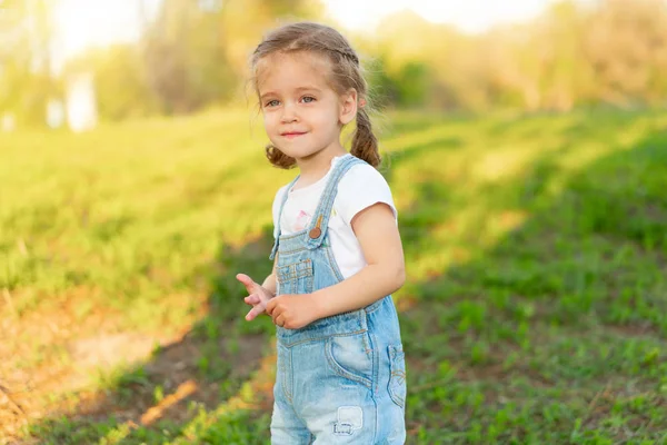 Kleine Kaukasische meisje wandelingen op de natuur gekleed in denim overalls — Stockfoto