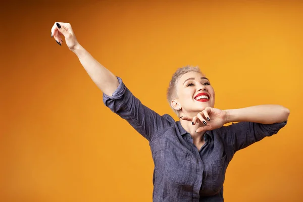 Portrait of young girl with blond short hairstyle looking at camera and laugh isolated on orange background with copy space — Stock Photo, Image
