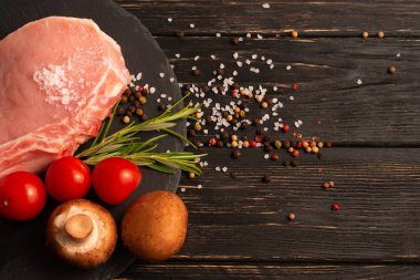 Siyah bir taş kesme tahtası üzerinde kiraz domates Champignon mantar ile bir adet çiğ domuz pirzolası biftek üst görünümü.