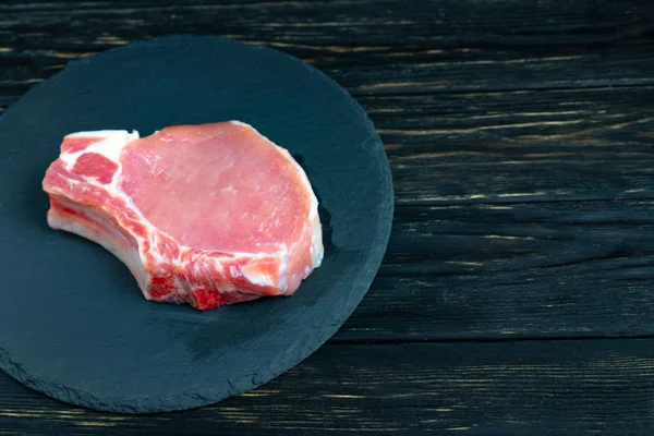 Siyah bir taş kesme tahtası üzerinde bir adet çiğ domuz pirzolası biftek üst görünümü.