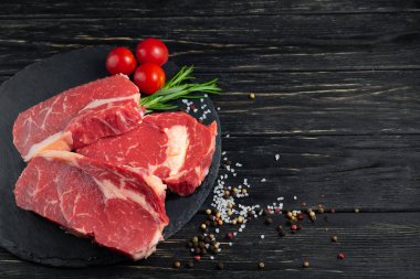 Siyah ahşap masa arka plan üzerinde bir taş kesme tahtası üzerinde sulu çiğ sığır eti üç adet.