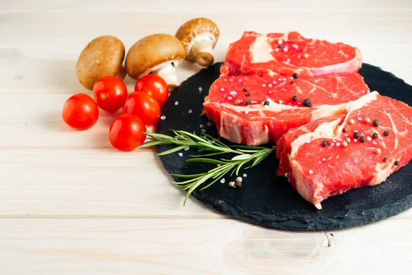 Drei Stücke saftigen rohen Rindfleisches auf einem Steinschneidebrett auf weißem Holztischhintergrund. — Stockfoto