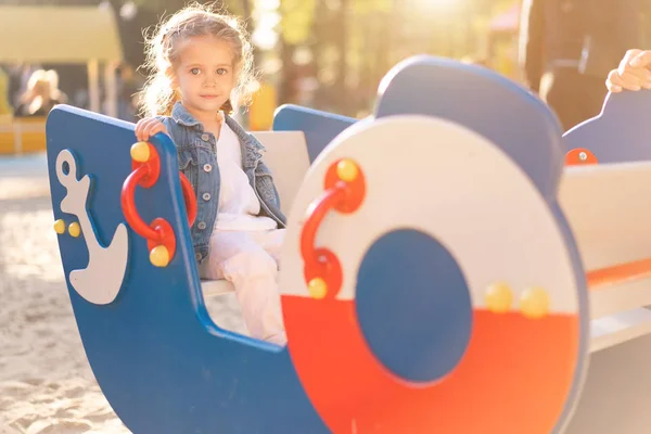Kleines kaukasisches Mädchen in Jeansjacke spielt an einem sonnigen Tag auf dem Spielplatz — Stockfoto
