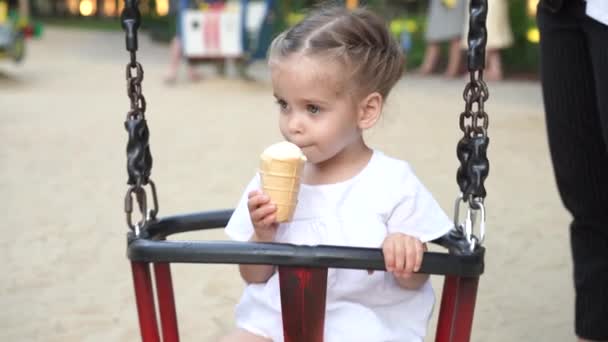 Маленькая девочка облизывает мороженое в вафельном рожке летом в парке с красивым закатом . — стоковое видео