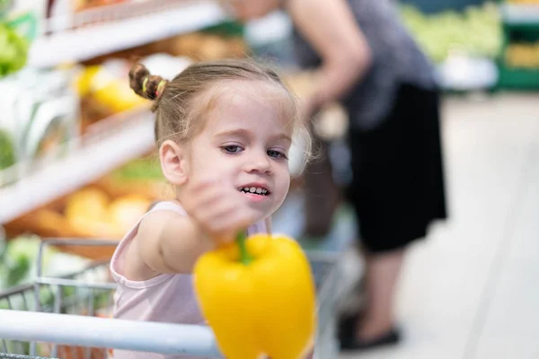 Mała kaukaski dziewczyna wybiera świeże warzywa w supermarkecie. — Zdjęcie stockowe