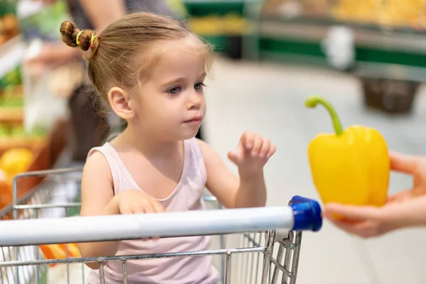 Mała kaukaski dziewczyna wybiera świeże warzywa w supermarkecie. — Zdjęcie stockowe