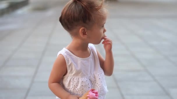 귀여운 백인 어린 소녀는 공원에서 걷는 와플 콘에서 아이스크림을 즐긴다. 아이가 밝은 아이스크림을 먹는다 — 비디오