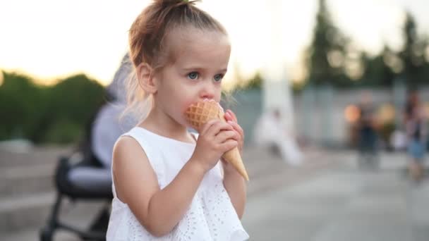 Aranyos kaukázusi kislány élvezi fagylaltot egy Waffle kúp séta a parkban. A gyermek eszik fényes fagylaltot — Stock videók