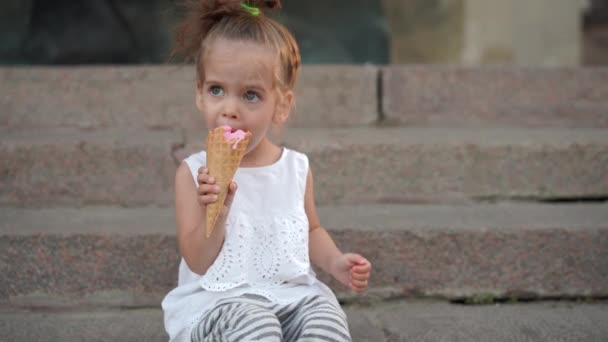 Menina branca bonito gosta de sorvete em um cone de waffle andando no parque. A criança come sorvete brilhante — Vídeo de Stock