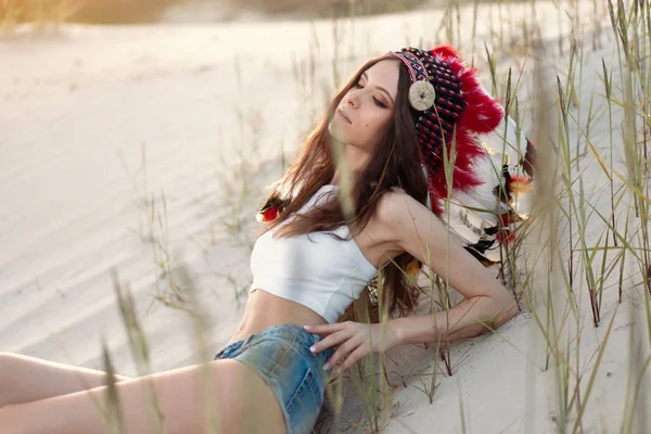 Uma linda jovem caucasiana em um top branco na cabeça está usando um chapéu indiano. O Roach está no deserto. Feliz clima de férias . — Fotografia de Stock