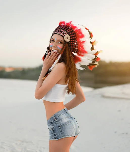 Ein schönes junges kaukasisches Mädchen in weißem Top und Jeanshosen. auf ihrem Kopf trägt eine Indianerhut-Rotauge. in der Wüste stehen. — Stockfoto