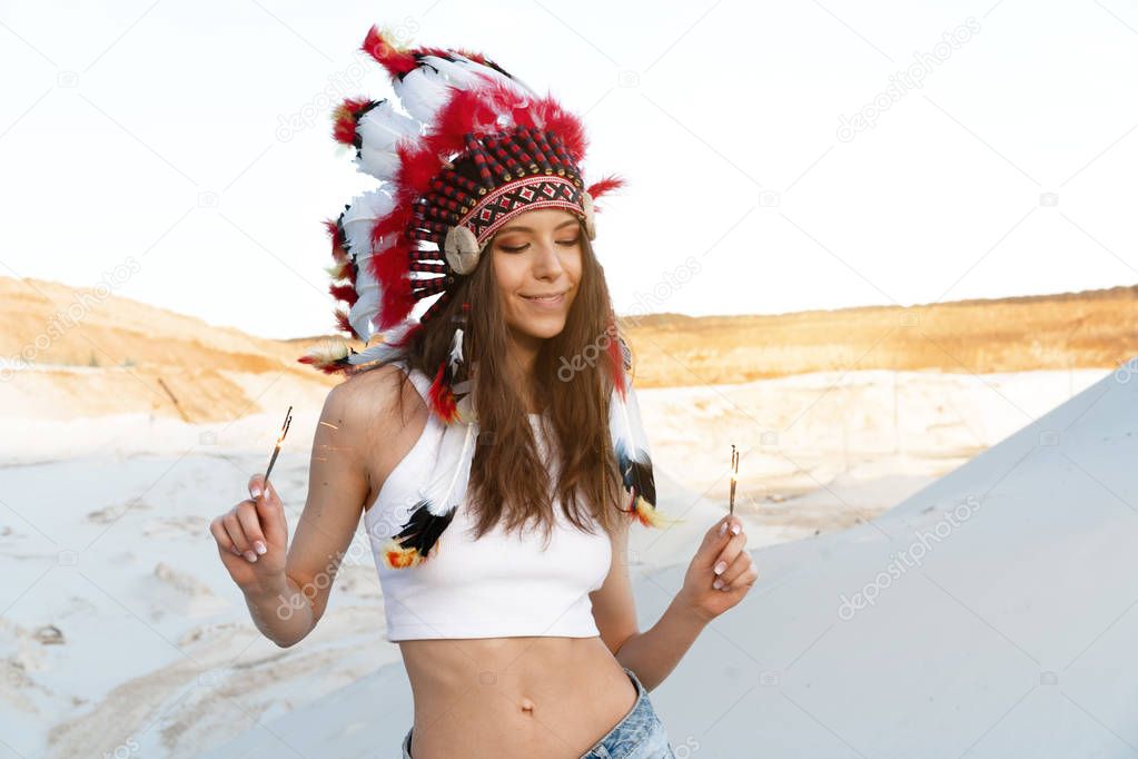 A beautiful young Caucasian girl in a white top on her head is wearing an Indian hat. Roach is in the desert. Happy holiday mood.