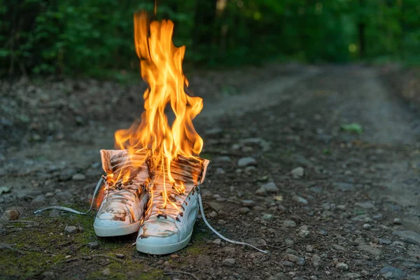 Used white high sneakers burning on a rural road that runs in the forest. — Stock Photo, Image