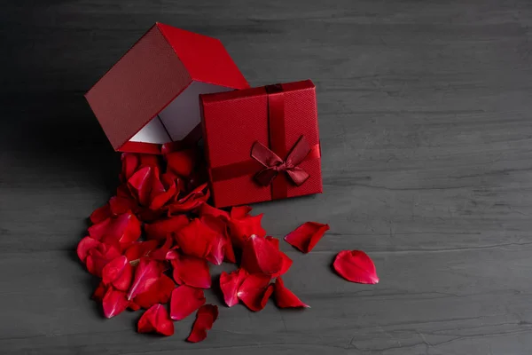 Beautiful red roses next to a gift red box on a dark cement background.