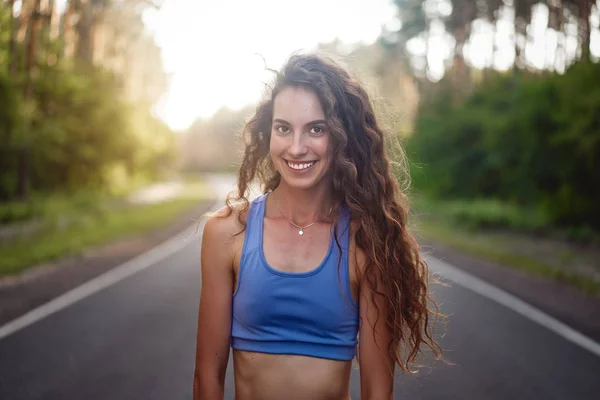 Beautiful young Caucasian girl  standing on asphalt forest road smiling before jogging. — Stock Photo, Image
