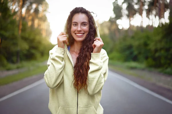 Beautiful young Caucasian girl  standing on asphalt forest road smiling after jogging. — Stock Photo, Image