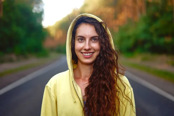 Beautiful young Caucasian girl  standing on asphalt forest road smiling after jogging. — Stock Photo, Image