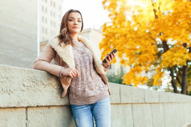 Güzel kafkas esmer kız sarı yeşillik ve bir şehir ile ağaçların arka plan ile sıcak sonbahar günü ayakta. Giyinmiş yün kazak ve ceket. 