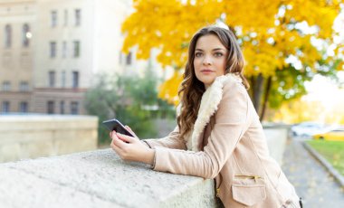 Güzel kafkas esmer kız sarı yeşillik ve bir şehir ile ağaçların arka plan ile sıcak sonbahar günü ayakta. Giyinmiş yün kazak ve ceket. 