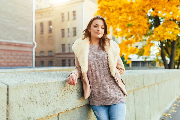 Beautiful caucasian brunette girl standing warm autumn day with background of trees with yellow foliage and a city. — Stock Photo, Image