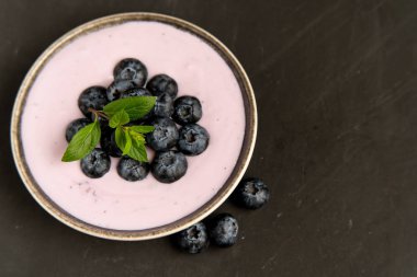 Siyah koyu masa arka planda duran seramik kase lezzetli taze yaban mersini yoğurt sallamak tatlı. 
