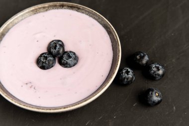 Siyah koyu masa arka planda duran seramik kase lezzetli taze yaban mersini yoğurt sallamak tatlı. 