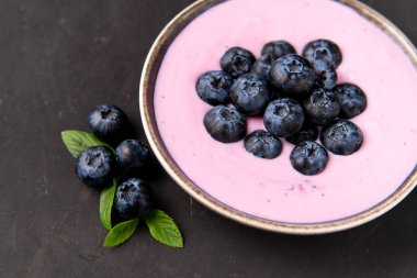 Siyah koyu masa arka planda duran seramik kase lezzetli taze yaban mersini yoğurt sallamak tatlı. 