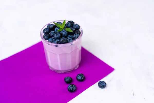 Sabroso yogur de arándano fresco agitar postre en vidrio de pie sobre fondo de servilleta púrpura mesa blanca . — Foto de Stock