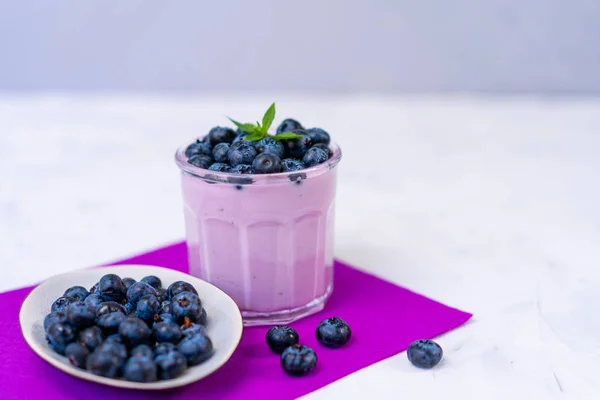 Sabroso yogur de arándano fresco agitar postre en vidrio de pie sobre fondo de servilleta púrpura mesa blanca . — Foto de Stock