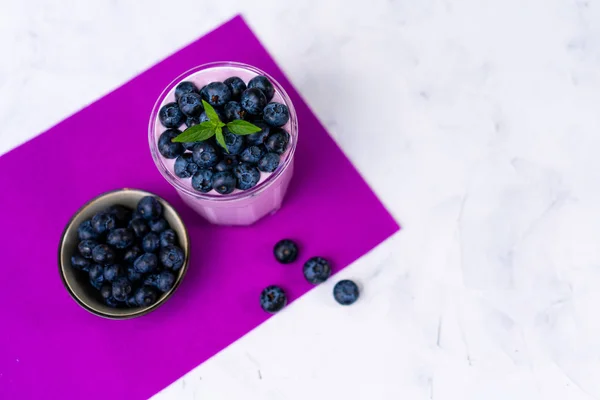 Sabroso yogur de arándano fresco agitar postre en vidrio de pie sobre fondo de servilleta púrpura mesa blanca . — Foto de Stock