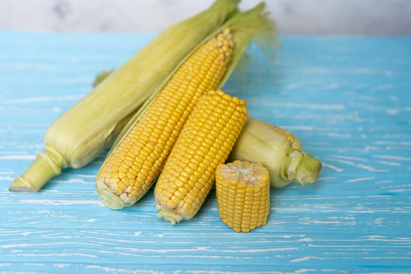 Corn cob with green leaves lies on table blue color background. — Stock Photo, Image