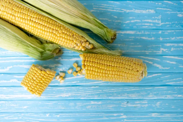 Corn cob with green leaves lies on table blue color background. — Stock Photo, Image