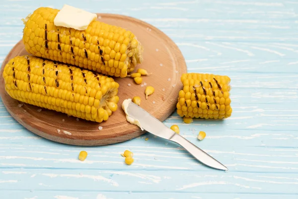 Grilled hot Corn cob lies on cutting board blue wooden table background. — Stock Photo, Image