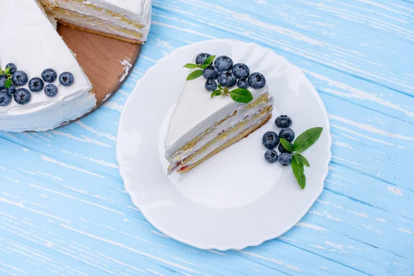 Appetizing cheesecake cake biscuit pillow decorated white cream blueberries and mint stands on wooden blue rustic table