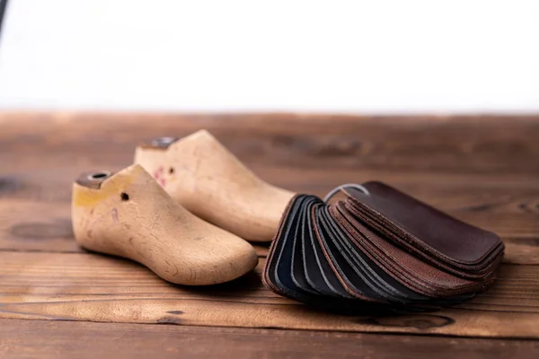 Kožené vzorky na boty a dřevěnou botu vydrží na tmavém dřevěném stole. — Stock fotografie