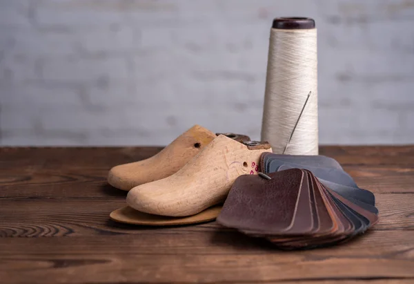 Leather samples for shoes and wooden shoe last on dark wooden table.