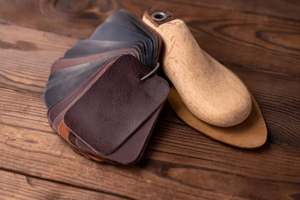 Kožené vzorky na boty a dřevěnou botu vydrží na tmavém dřevěném stole. — Stock fotografie