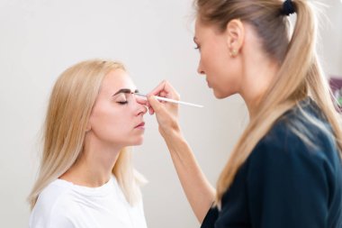 Kozmetik dolabı müşterisi koltukta oturuyor. Güzellik uzmanı kaşlara işaret koyuyor.