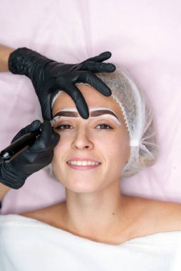 Kozmetik dolabı müşterisi kanepede yatıyor. Güzellik uzmanı kaşlara işaret koyuyor.