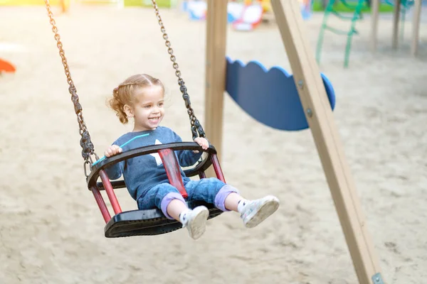 Little Caucasian girl riding swing at playground sunny summer day. — Stock Photo, Image