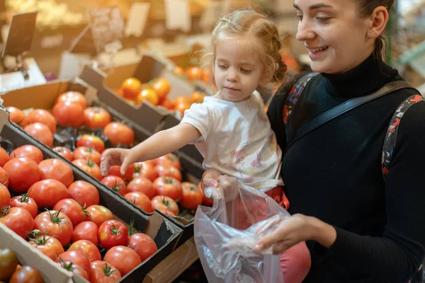 Joyeux sourire jeune femme avec petite fille achetant des tomates rouges au marché — Photo