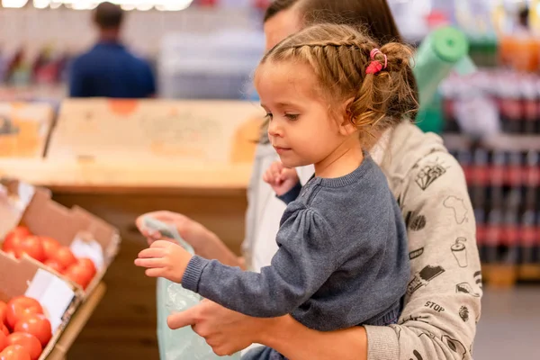 Joyeux sourire jeune femme avec petite fille achetant des tomates rouges au marché — Photo