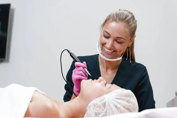 Cosmetology cabinet client lies on couch. Beautician applies marking on eyebrows. — Stock Photo, Image