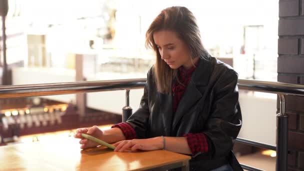 Νεαρή όμορφη Καυκάσια κοπέλα κάθεται σε ένα καφέ κοιτάζοντας την οθόνη του τηλεφώνου παίρνει άσχημα νέα και είναι αναστατωμένος. — Αρχείο Βίντεο