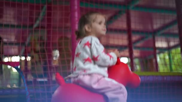 Ein süßes kleines kaukasisches Mädchen spielt auf dem Spielplatz, reitet im Sommer auf einem Gummipferd. — Stockvideo