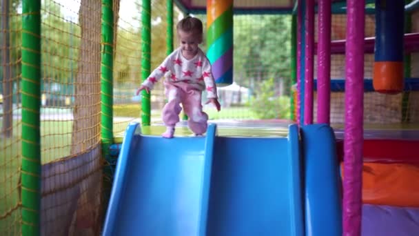 Liten flicka unge går ner från plast glider till bollarna på en lekplats — Stockvideo