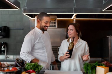 Yakışıklı genç Afrikalı şef, beyaz kız arkadaşıyla mutfakta yemek pişiriyor. Kırmızı şarabı malzeme olarak kullanıyor..