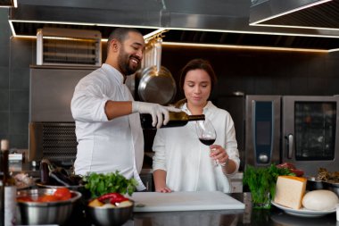 Yakışıklı genç Afrikalı şef, beyaz kız arkadaşıyla mutfakta yemek pişiriyor. Kırmızı şarabı malzeme olarak kullanıyor..