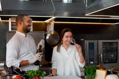 Yakışıklı genç Afrikalı şef, beyaz kız arkadaşıyla mutfakta yemek pişiriyor. Kırmızı şarabı malzeme olarak kullanıyor..