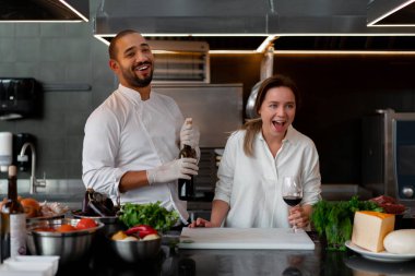 Yakışıklı genç Afrikalı şef, beyaz kız arkadaşıyla mutfakta yemek pişiriyor. Kırmızı şarabı malzeme olarak kullanıyor..